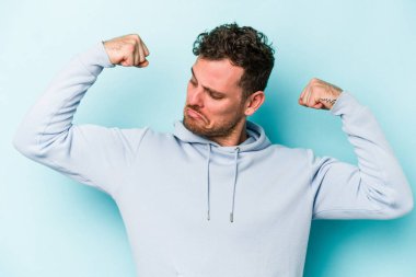 Mavi arka planda izole edilmiş genç beyaz adam güçlü bir hareket sergiliyor kollarıyla, kadınsı gücün sembolü.