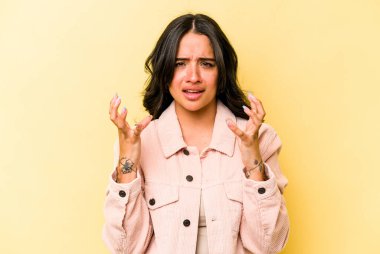 Sarı arka planda izole edilmiş genç İspanyol kadın gergin elleriyle çığlık atıyor..