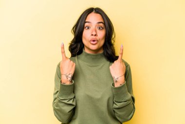 Sarı arka planda izole edilmiş, ağzı açık, üst tarafı işaret eden genç İspanyol kadın..