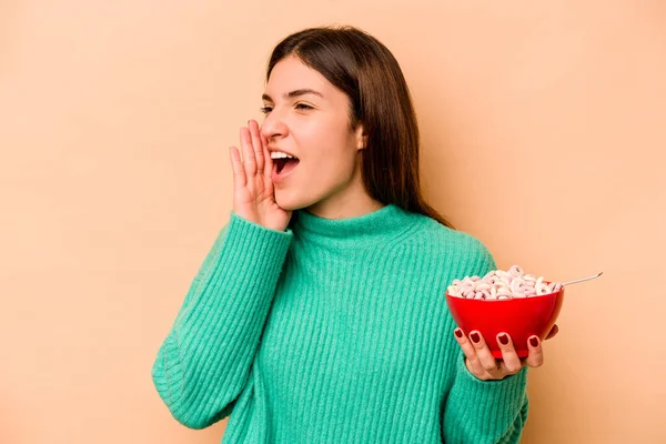 Jonge Spaanse Vrouw Eten Granen Geïsoleerd Beige Achtergrond Schreeuwen Houden — Stockfoto