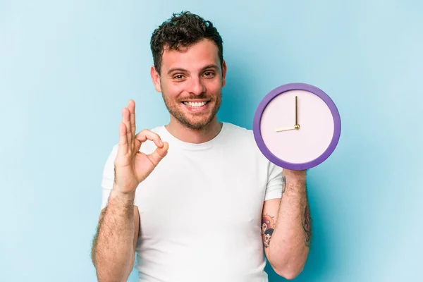 Jonge Blanke Man Met Een Klok Geïsoleerd Blauwe Achtergrond Vrolijk — Stockfoto