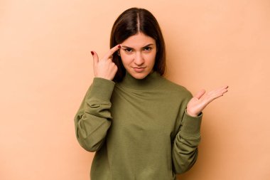 Genç İspanyol kadın bej arka planda izole edilmiş işaret parmağıyla hayal kırıklığı jesti gösteriyor..