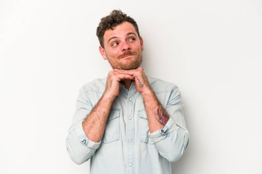 Beyaz arka planda izole genç beyaz adam ellerini çenesinin altında tutuyor, mutlu bir şekilde yana bakıyor..