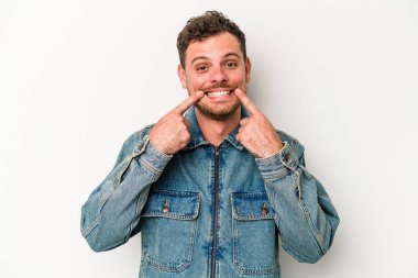 Beyaz arka planda izole edilmiş genç beyaz adam gülümsüyor, parmaklarını ağıza doğrultuyor..
