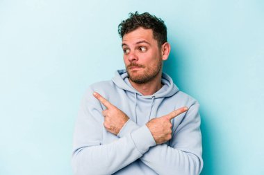 Mavi arka plan noktalarında izole genç beyaz adam, iki seçenek arasında seçim yapmaya çalışıyor.