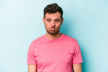 Kafkasyalı genç adam mavi arka planda izole edilmiş üzgün, ciddi yüzlü, mutsuz ve hoşnutsuz..