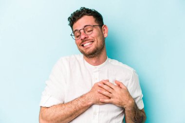 Mavi arka planda izole edilmiş beyaz bir genç, dost bir ifadeye sahip, avuçlarını göğsüne bastırıyor. Aşk konsepti.