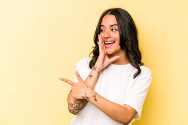 Latin kökenli genç bir kadın sarı arka planda izole edilmiş. Dedikodu yapıyor, bir şeyleri bildiriyor..