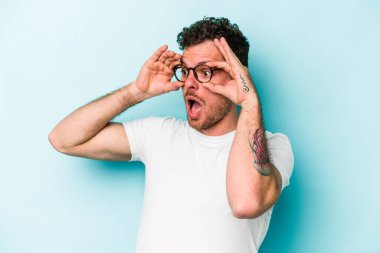 Mavi arka planda izole edilmiş genç beyaz adam bir başarı fırsatı bulmak için gözlerini açık tutuyor..