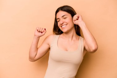 Latin kökenli genç bir kadın bej arka planda izole edilmiş özel bir günü kutluyor, atlıyor ve enerjiyle kollarını kaldırıyor..