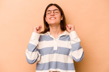 Genç İspanyol kadın bej arka planda izole edilmiş zafer, tutku ve coşkuyu kutluyor, mutlu bir ifade..