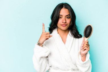 Mavi arka planda saç fırçası tutan genç İspanyol kadın bir numarayı parmağıyla gösteriyor..