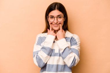 Latin kökenli genç bir kadın bej arka planda izole edilmiş. İki seçenek arasında şüphe duyuyor..