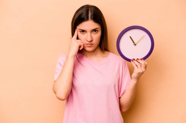 Elinde bej arka planda izole edilmiş bir saat tutan genç İspanyol kadın parmağıyla tapınağı işaret ediyor, düşünüyor ve bir göreve odaklanıyor..