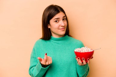 Latin kökenli genç bir kadın bej arka planda yalıtılmış mısır gevreği yiyor. Sanki seni davet ediyormuş gibi seni işaret ediyor..