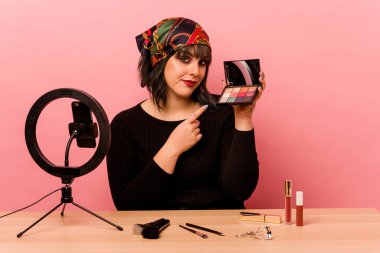 Makyaj sanatçısı genç bir kadın pembe arka planda özel bir makyaj dersi veriyor.