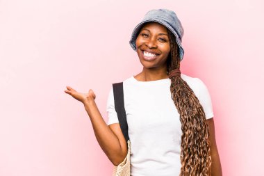 Genç Afrikalı Amerikalı bir kadın pembe arka planda izole edilmiş bir şekilde sahile gidiyor. Bir avuç içinde fotokopi alanı ve belinde bir el daha gösteriyor..