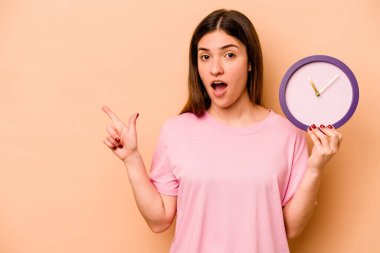 Elinde bej arka planda izole edilmiş bir saat tutan genç İspanyol kadın yan tarafı işaret ediyor.