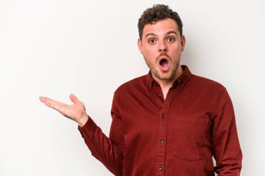 Beyaz arka planda izole edilmiş genç beyaz adam, avuç içi fotokopi alanını elinde tutmaktan etkilenmiş..