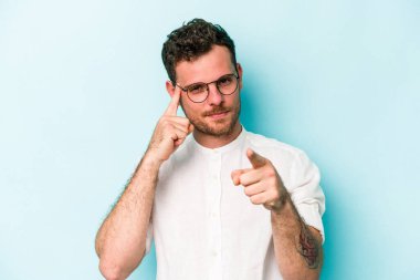 Mavi arka planda izole edilmiş genç beyaz bir adam şakağı parmağıyla işaret ediyor, düşünüyor ve bir göreve odaklanıyor..