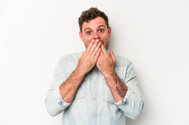 Beyaz arka planda izole edilmiş genç beyaz adam şok olmuş, ağzı ellerle kaplanmış, yeni bir şey keşfetmeye hevesli..