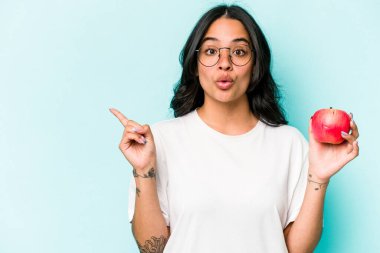 Mavi arka planda izole edilmiş bir elma tutan genç İspanyol kadın...