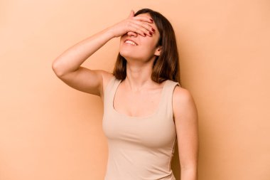 Latin kökenli genç bir kadın, bej arka planda izole edilmiş, mutlu bir şekilde ellerini başının üstünde tutarak gülüyor. Mutluluk kavramı.