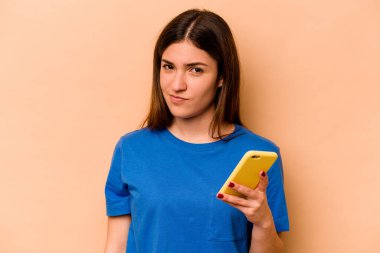 Elinde cep telefonu olan beyaz bir kadın bej arka planda izole edilmiş.