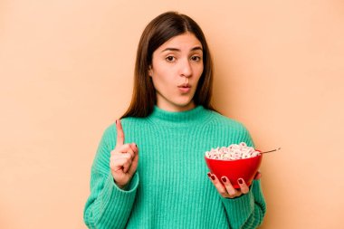 Latin kökenli genç bir kadın bej arka planda izole edilmiş mısır gevreği yiyor. Harika bir fikri var, yaratıcılık kavramı..