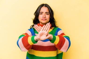Sarı arka planda izole edilmiş genç İspanyol kadın elini uzatmış, dur işareti göstererek seni engelliyor..