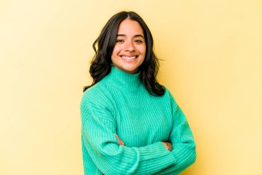 Sarı arka planda izole edilmiş, kendinden emin, kararlılıkla kollarını kavuşturan genç İspanyol kadın..