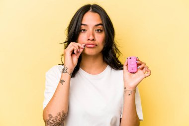 Pembe arka planda izole edilmiş anahtar taşıyan genç İspanyol kadın dudaklarında bir sır saklıyor..