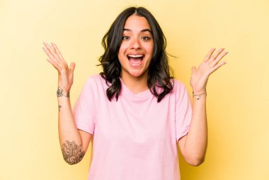 Sarı arka planda izole edilmiş genç İspanyol kadın hoş bir sürprizle karşılaşıyor, heyecanlı ve el kaldırıyor..