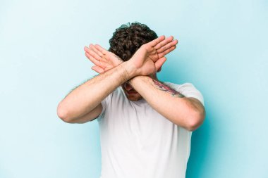 Kafkasyalı genç adam mavi arka planda izole edilmiş iki kolu çapraz tutuyor, inkar kavramı.