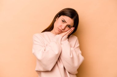 Latin kökenli genç bir kadın bej arka planda izole edilmiş. Esniyor. Ağzı eliyle kapatan yorgun bir jest gösteriyor..