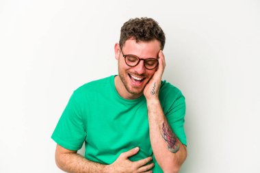 Beyaz arka planda izole genç beyaz adam mutlu bir şekilde gülüyor ve ellerini karnının üstünde tutarak eğleniyor..