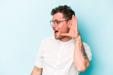 Mavi arka planda izole edilmiş genç beyaz adam bir dedikoduyu dinlemeye çalışıyor..