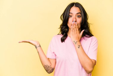 Sarı arka planda izole edilmiş genç İspanyol kadın avuç içi fotokopi alanını tutmaktan etkilenmiş..