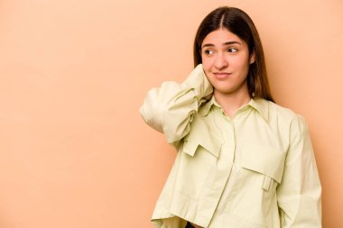 Genç İspanyol kadın bej arka planda izole edilmiş kafasının arkasına dokunuyor, düşünüyor ve bir seçim yapıyor..