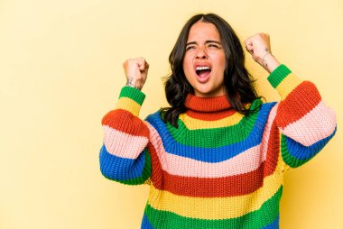 Sarı arka planda izole edilmiş genç İspanyol kadın zaferden sonra yumruk kaldırıyor, kazanan konsept..