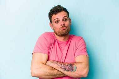 Mavi arka planda izole edilmiş genç beyaz adam omuzlarını silkeliyor ve gözleri açık..