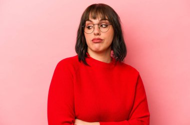 Pembe arka planda izole edilmiş genç beyaz kadın alaycı bir ifadeyle kameraya bakıyor..