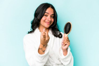 Mavi arka planda saç fırçası tutan genç İspanyol kadın sanki seni davet ediyormuş gibi seni işaret ediyor..