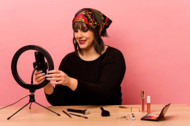 Makyaj sanatçısı genç bir kadın pembe arka planda özel bir makyaj dersi veriyor.