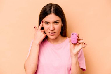 Latin kökenli genç bir kadın, elinde bej arka planda izole edilmiş bir araba tutarken işaret parmağıyla yaptığı hayal kırıklığı jestini gösteriyor..