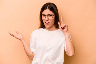 Latin kökenli genç bir kadın bej arka planda izole edilmiş ve elinde bir ürün tutuyor..