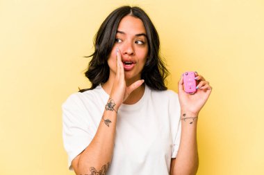 Pembe arka planda izole edilmiş anahtar taşıyan genç İspanyol kadın gizli bir sıcak fren haberi veriyor ve yana bakıyor.