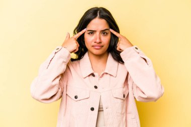 Sarı arka planda izole edilmiş genç İspanyol kadın bir işe odaklanmış, işaret parmaklarını işaret ediyor..