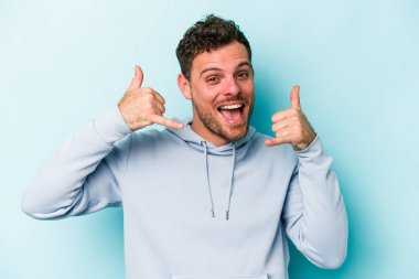 Mavi arka planda izole edilmiş genç beyaz adam parmaklarıyla bir cep telefonu hareketi gösteriyor..