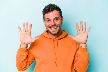 Mavi arka planda izole edilmiş genç beyaz adam on numarayı elleriyle gösteriyor..